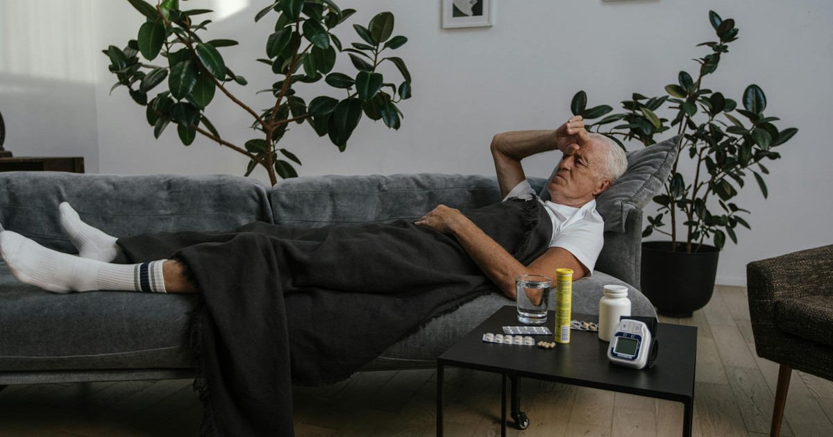 Senior man resting on a couch indoors with medicines on the table, looking unwell.