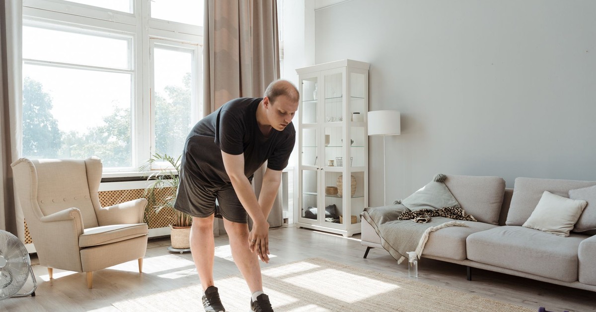 Man performing a stretching exercise in a sunlit living room, embracing a healthy lifestyle.