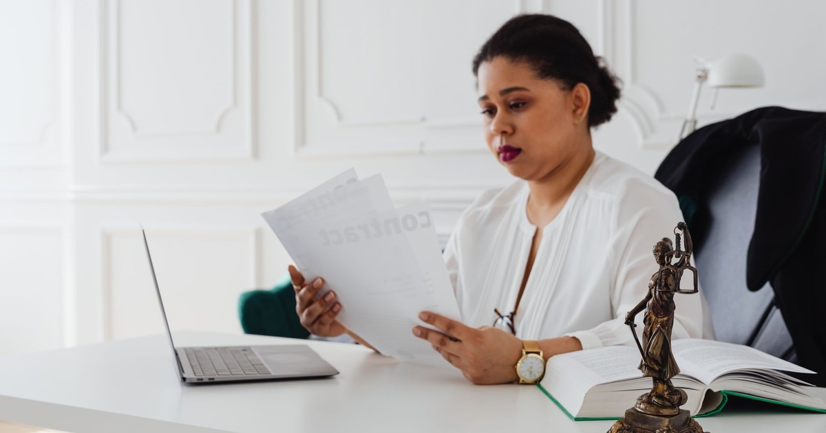Black woman lawyer reading legal papers at her desk in a modern office.