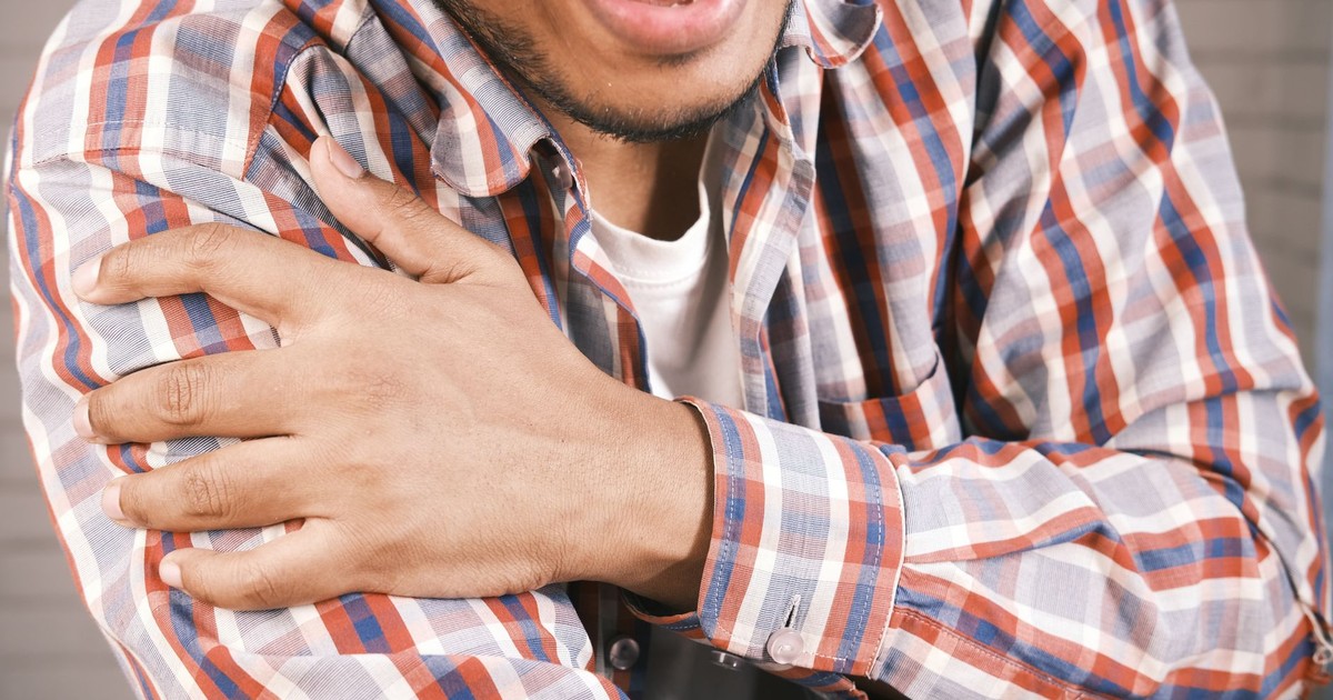 Close-up of a man in plaid shirt experiencing shoulder pain, grasping his arm.