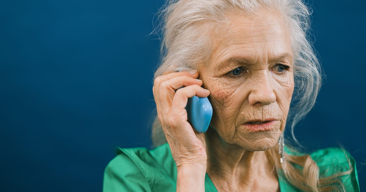 Senior woman with gray hair talks on mobile phone against a blue background.