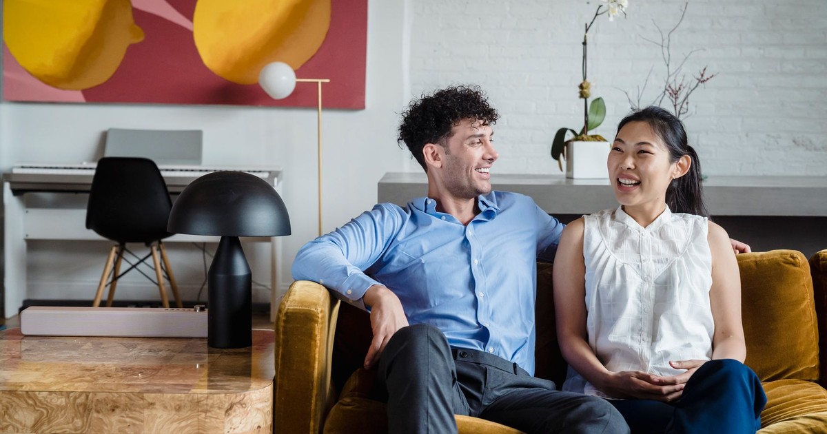 Asian woman and caucasian man laughing on a couch in a stylish living room setting.