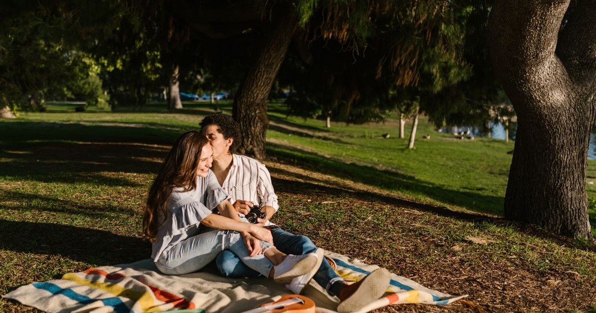 Young couple sharing a romantic picnic in a lush green park under the trees.