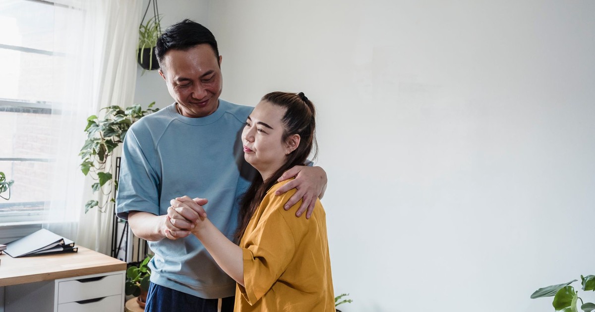 Couple sharing a tender moment and dancing together in a bright, plant-filled living room.