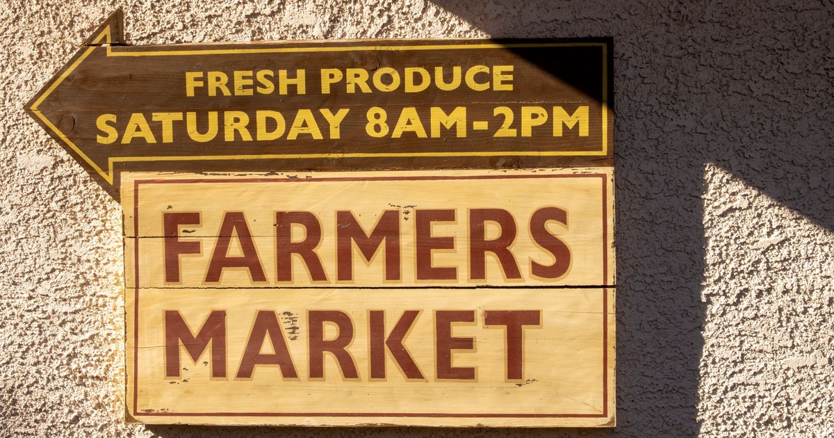 Brightly painted farmers market sign indicating fresh produce times.