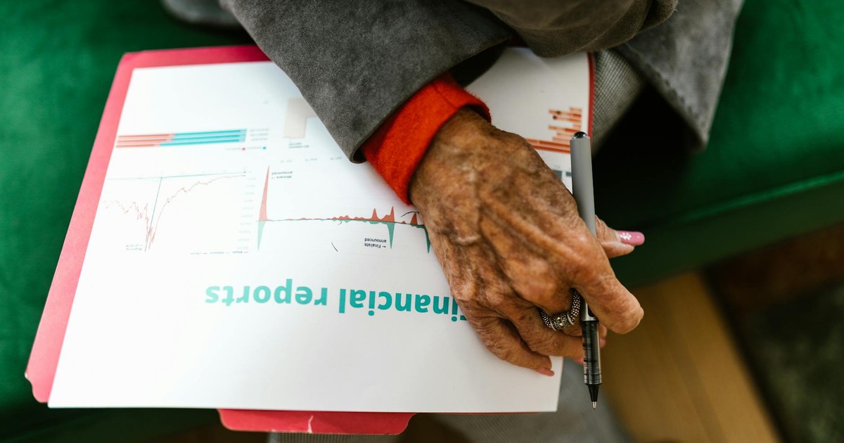 Close-up of an elderly woman holding a pen with a financial report.