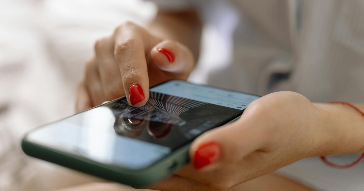 A person with red nails using a smartphone with a touch screen interface.