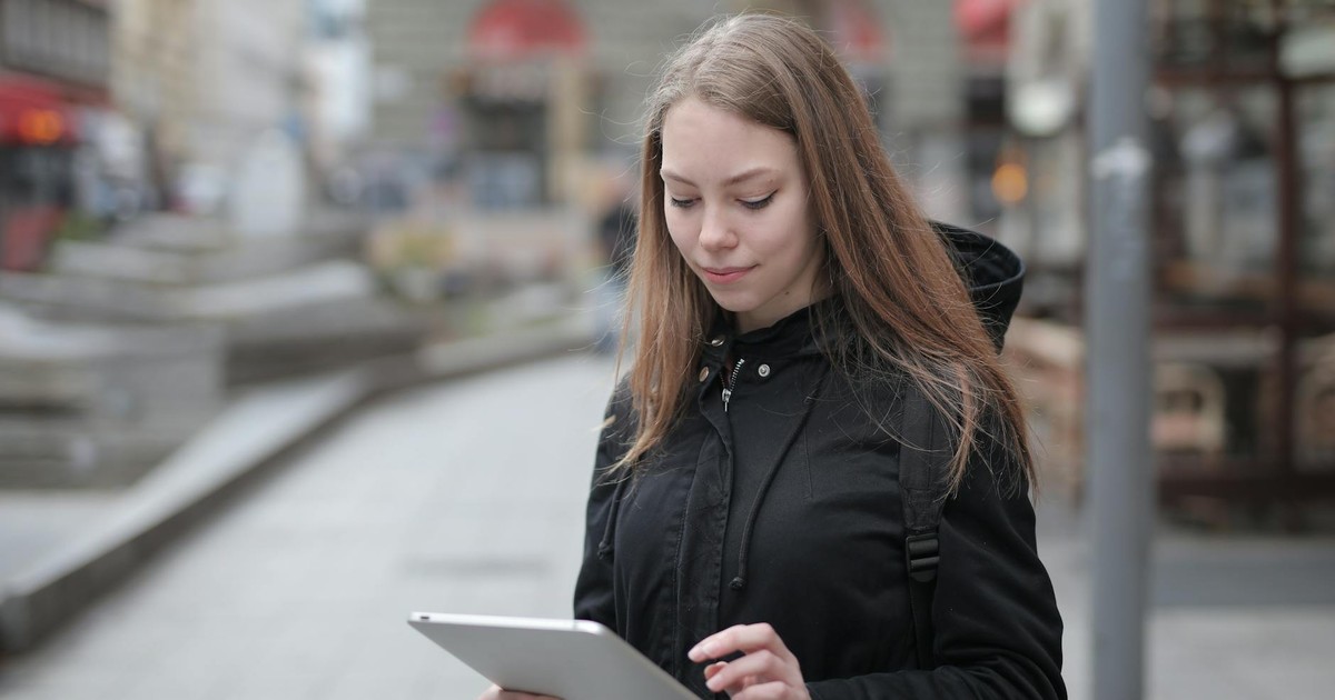 A young woman using a tablet outdoors in a city street, portraying modern lifestyle and technology.