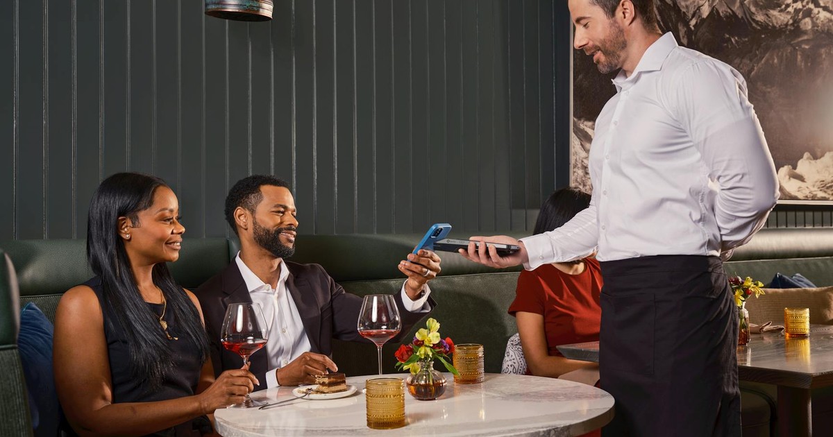 Diners complete a contactless payment in a sophisticated restaurant with a handheld POS system.