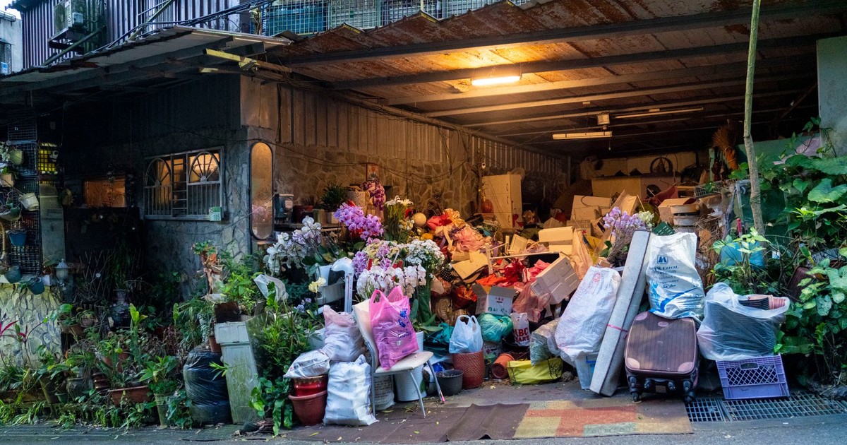 A garage filled with various household items, plants, and clutter overflowing onto the street.