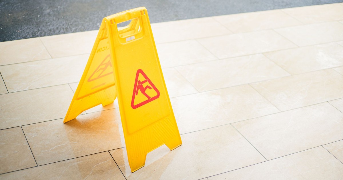 A bright yellow caution sign placed on a tile floor indicating a wet area for safety.
