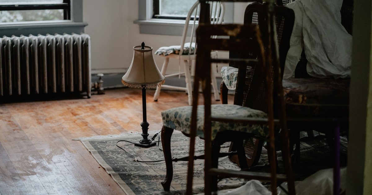 A dimly lit indoor space featuring an array of disorganized furniture and a vintage lamp.