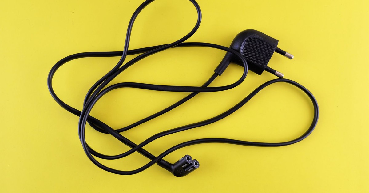 Close-up of a tangled black power cord placed on a vibrant yellow background.