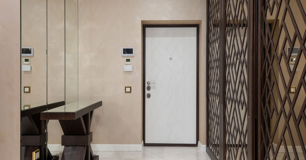 Elegant hallway interior featuring mirrors, modern door, and stylish furniture in neutral tones.