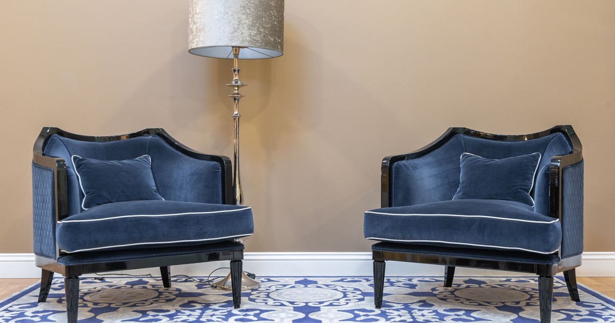 Pair of luxurious blue velvet chairs and a decorative lamp against a neutral wall.