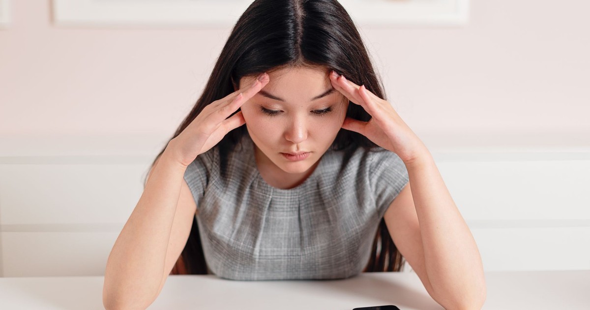 Asian businesswoman with a headache at her desk, displaying stress and anxiety.