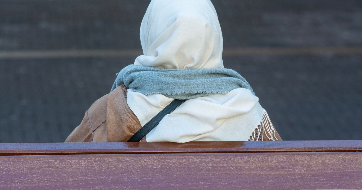 Back view of a woman wearing a headscarf sitting quietly on an outdoor bench.