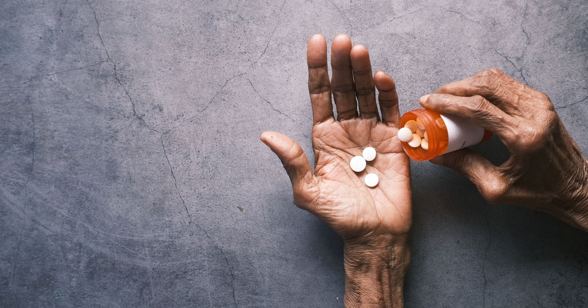 Elderly person's hand pouring pills from a bottle, offering ample copy space.