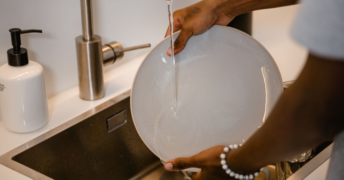 A close-up view of a person washing a plate in a modern kitchen sink with water running from the faucet.