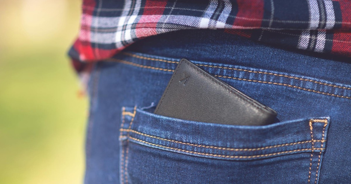 A wallet resting in the back pocket of denim jeans with a plaid shirt outdoors.