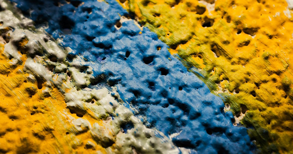 Close-up shot of a brightly painted textured surface featuring blue, yellow, and green hues.