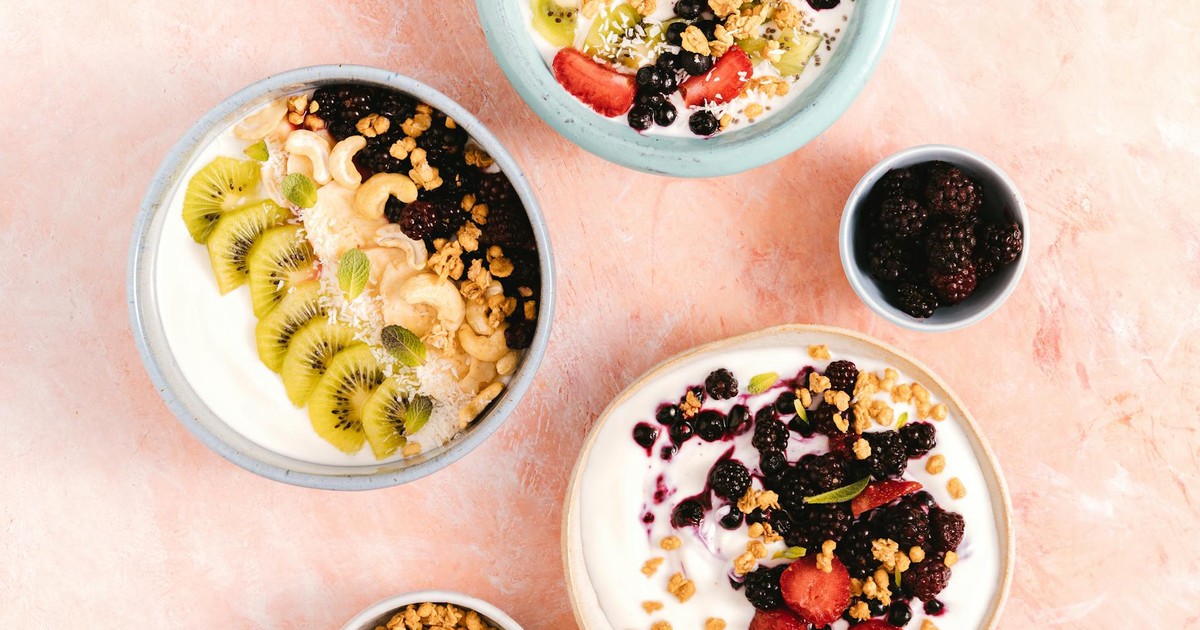 Top view of yogurt bowls topped with fresh fruits and nuts on a textured background.