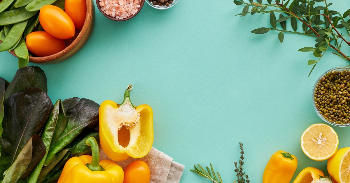 Vibrant flat lay of fresh vegetables, herbs, and spices on a teal background.