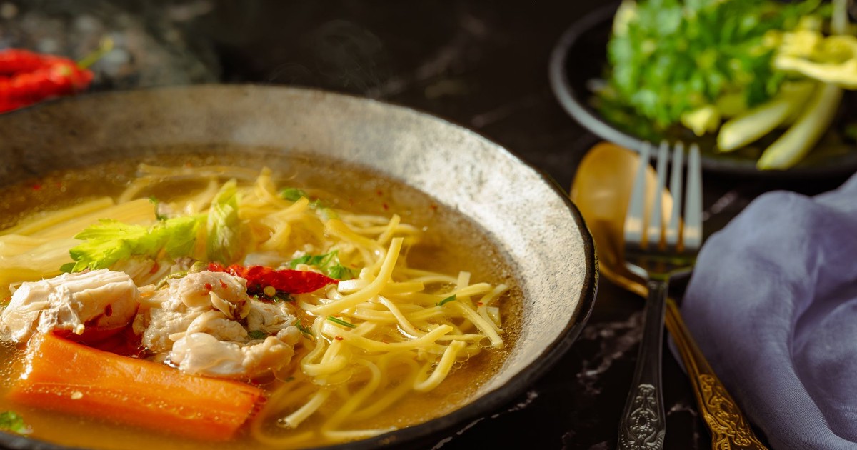 Capture of a flavorful chicken noodle soup with garnishes in a rustic setting.