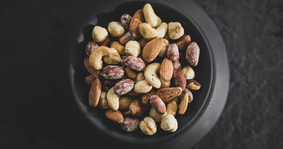 Top view of a variety of mixed nuts in a black bowl, showcasing almonds, cashews, and hazelnuts.