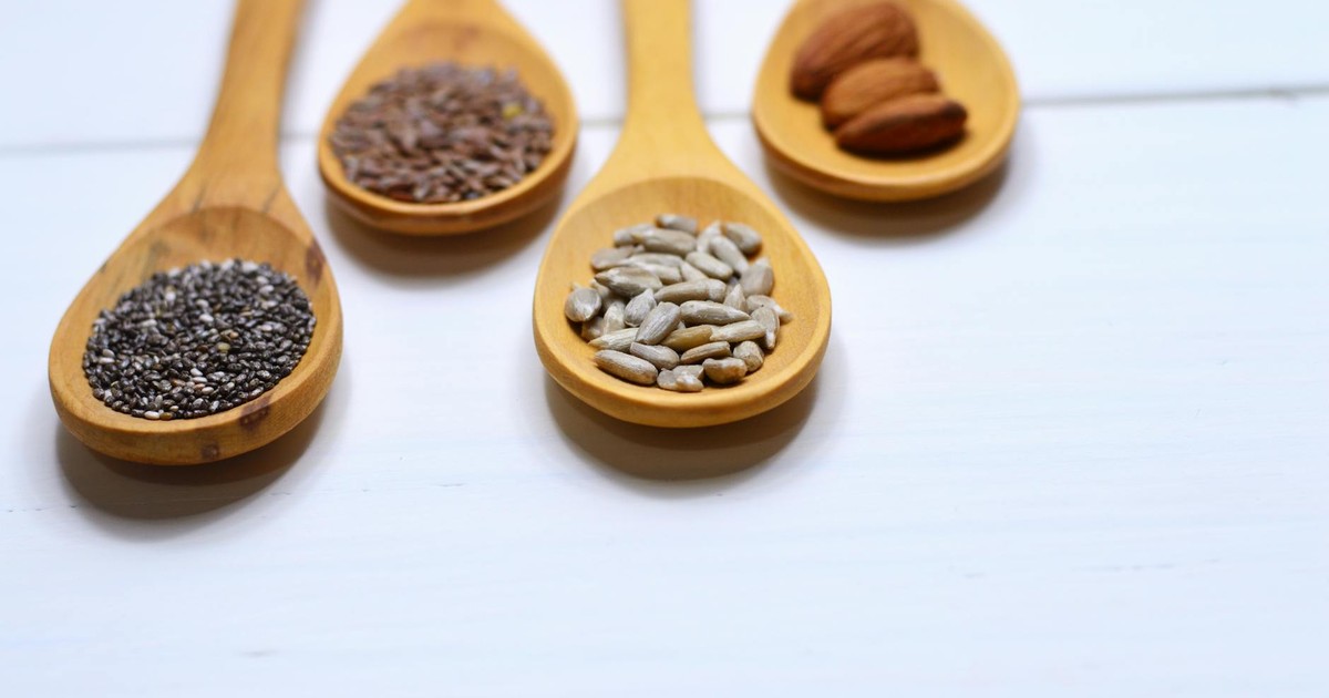 Close-up of various nuts and seeds in wooden spoons on a white background, showcasing healthy food options.