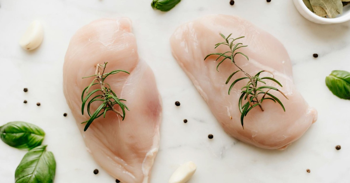 Close-up of raw chicken breasts garnished with rosemary on a marble surface with herbs and spices.