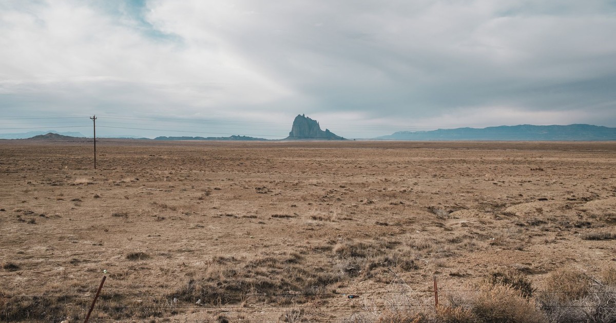 Expansive desert view of Shiprock in New Mexico, USA, under a cloudy sky.