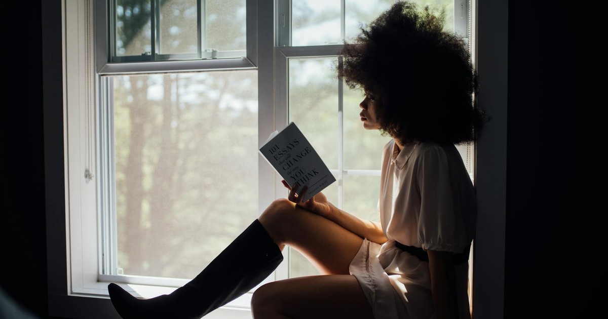 A woman enjoys a peaceful reading session by a window, bathed in natural light.