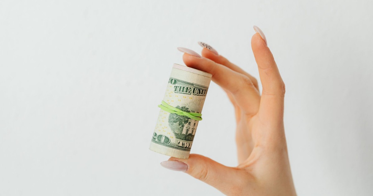 Close-up image of a hand holding a roll of US dollar bills with a rubber band.