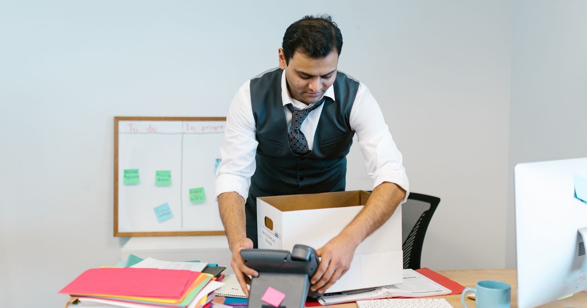 A man packing up his desk in an office setting with papers and a phone.