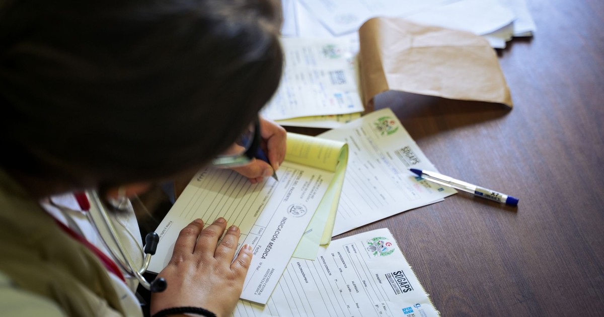 A doctor fills out medical forms indoors, focusing on patient care and documentation.