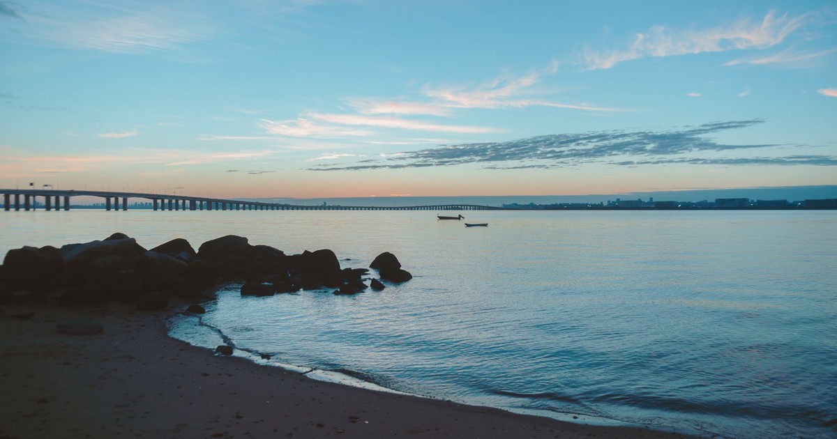 Serene beach sunset with a distant bridge and calm waters, ideal for relaxation themes.
