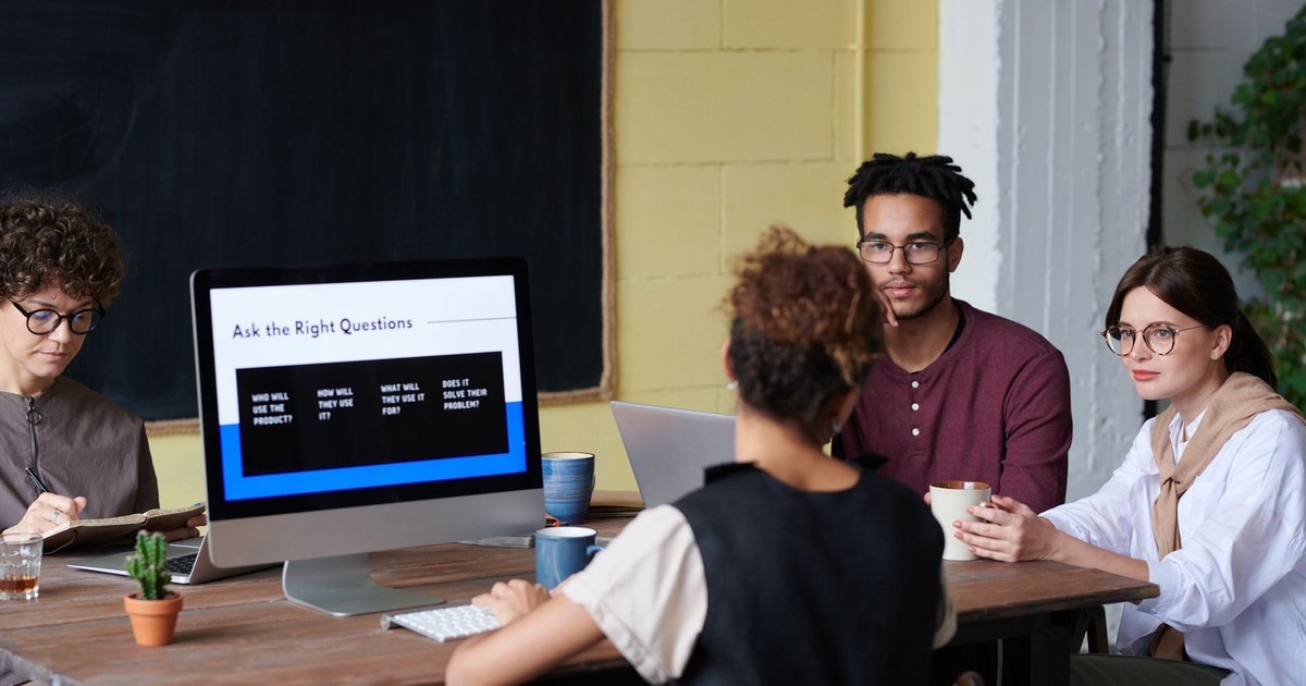 Group of diverse professionals discussing ideas in a modern office setting with computer screen prompts.