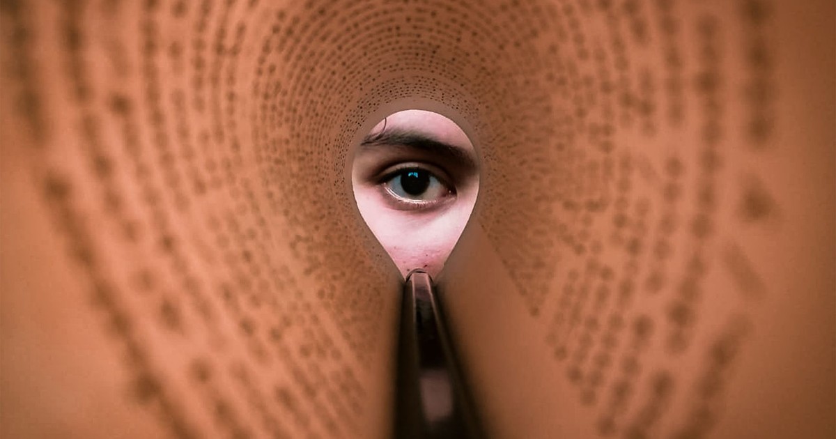 A person's eye looking through a rolled book page, creating a unique viewpoint.