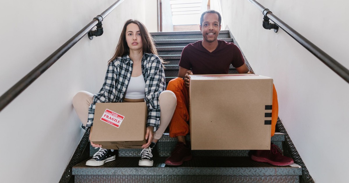 Interracial couple sitting on stairs with cardboard boxes, ready for moving.