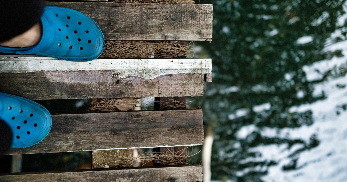 Close-up of feet in blue shoes on a wooden bridge above water.
