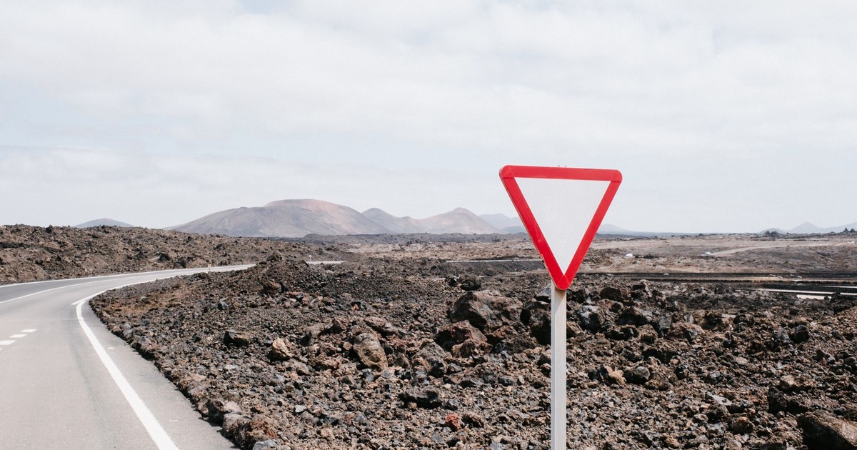 A deserted road in a rocky landscape with a yield sign under a cloudy sky.