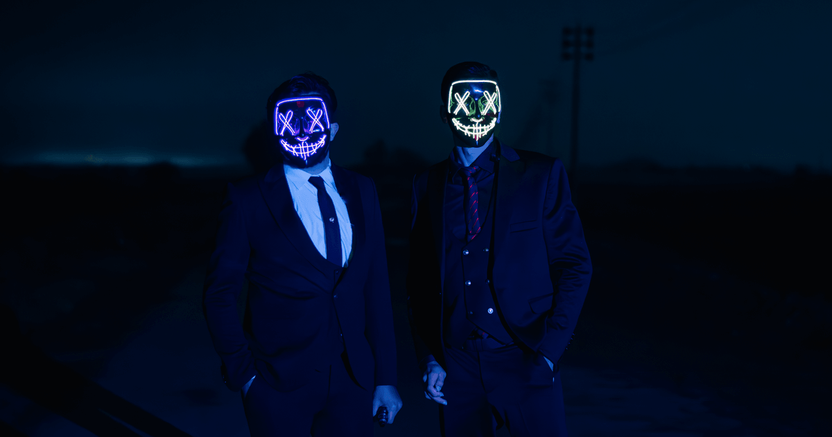 Two individuals in suits wearing illuminated LED masks under a dark night sky.