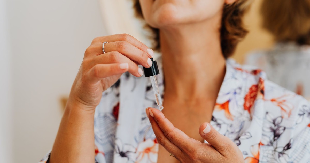 Close-up of a woman in a floral robe applying facial serum using a dropper.