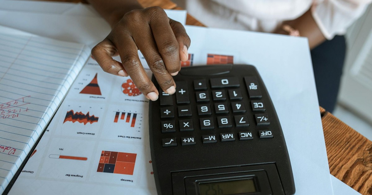 Person using calculator on desk with financial charts and graphs, ideal for business and finance themes.