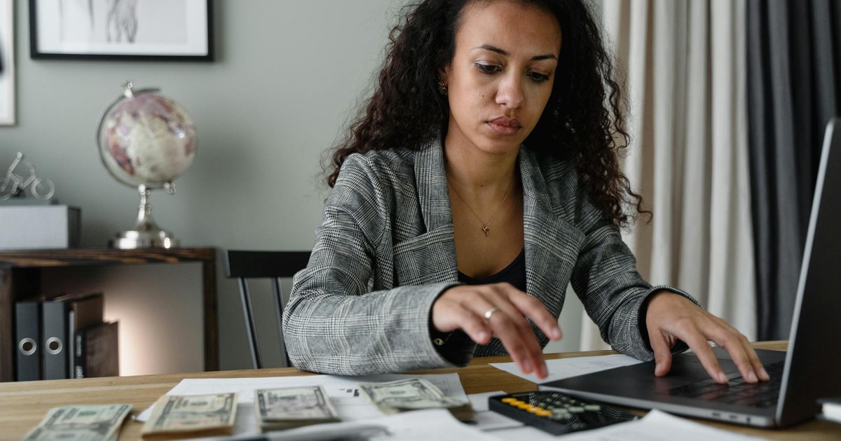 Professional woman analyzing financial documents and counting cash at office desk.