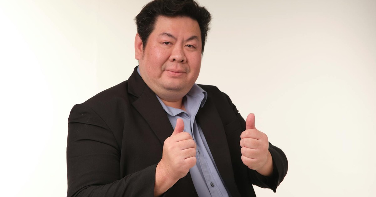 Business professional in dark suit giving thumbs up gesture in studio setting.