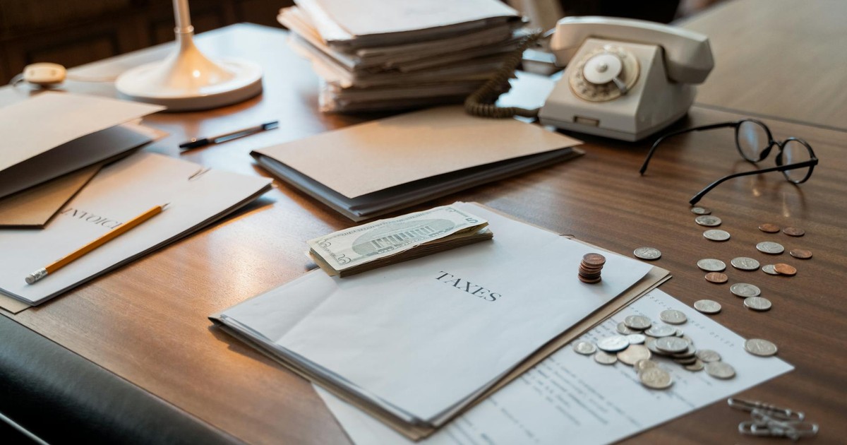 Close-up of an office desk with tax documents, coins, glasses, and an old phone, symbolizing finance and organization.
