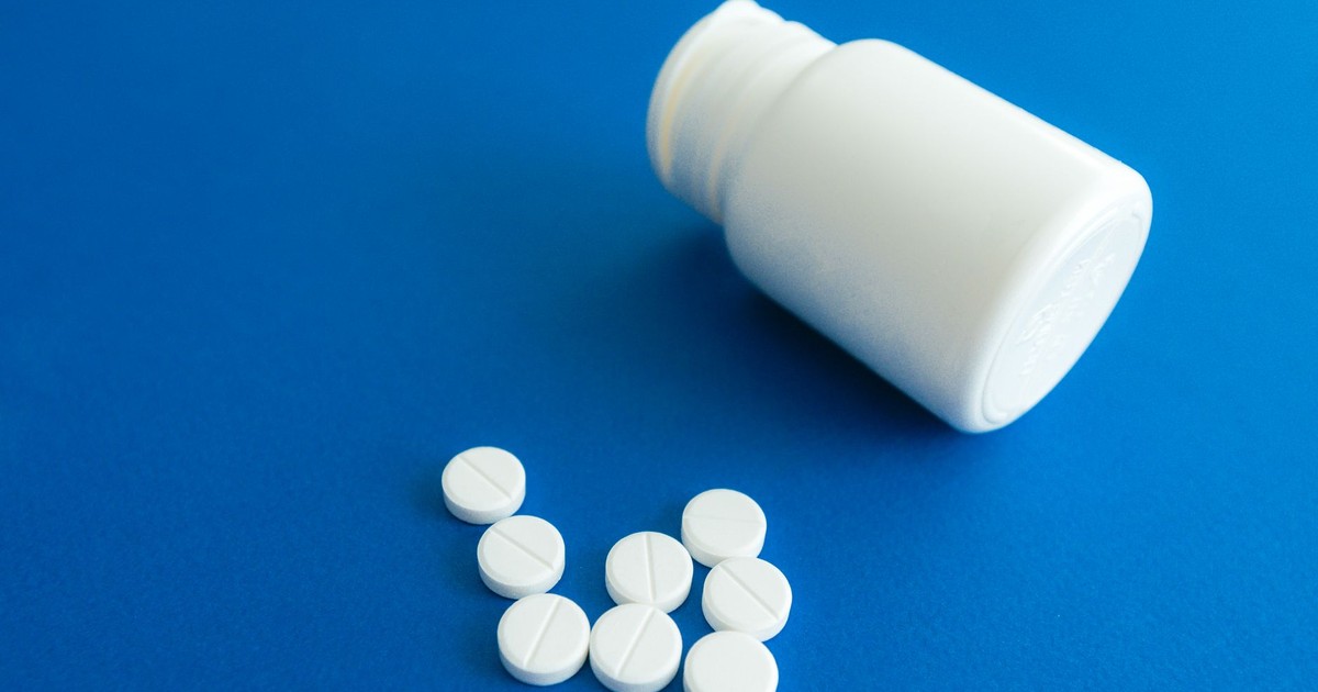 White tablets spilling from a plastic container on a solid blue background.