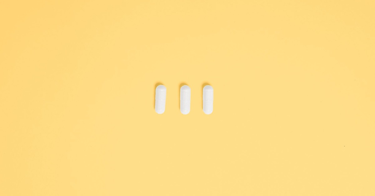 Three white capsules on a vibrant yellow background, symbolizing healthcare and medication.